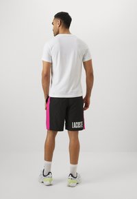 Balta kokvilnas T-kreklā, apvienota ar melniem šortiem ar rozā sānu paneļiem un baltu "LACOSTE" logo. Gadījuma sportiskais stils ar kontrastējošām krāsām.
