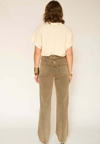 T-shirt beige oversize et pantalon marron en velours côtelé taille haute à jambes larges, avec poches arrière, tissu texturé et design épuré.