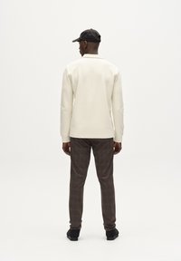 Pullover a collo rotondo di colore crema lavorato a maglia con maniche lunghe, abbinato a pantaloni a quadri marroni e scarpe nere, visto da dietro.