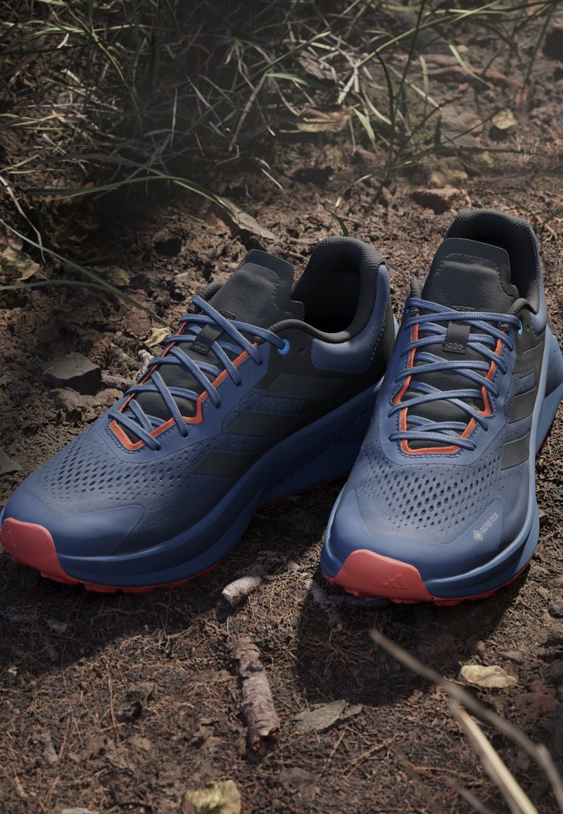 Scarpe da ginnastica blu con una tomaia testurizzata, dettagli neri e lacci arancioni. Presentano una punta rinforzata e una suola imbottita.