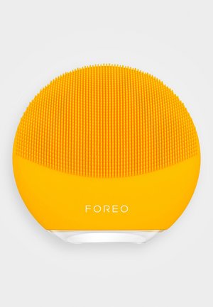 Siliconen gezichtsreinigingsapparaat, ronde vorm, felgeel, met textuur en kleine ribbels, met het merkembleem "FOREO" aan de voorkant.