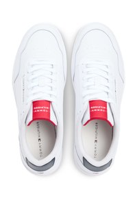 Άσπρα αθλητικά παπούτσια με λείο υλικό, στρογγυλεμένο σχήμα και λογότυπο σε κόκκινο και μπλε στο γλώσσο. Υποδήματα με υφή και διάτρητες λεπτομέρειες.