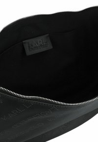 Schwarze Leder-Reisetasche mit Reißverschluss, die eine strukturierte Oberfläche und eingestanzte Logos aufweist. Das Innere ist mit schwarzem Stoff gefüttert und hat keine Taschen.