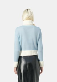 Maglione azzurro chiaro a taglio corto con colletto e polsini a coste bianchi. Presenta un design a maglia testurizzata e una vestibilità comoda. Gonna nera sotto.