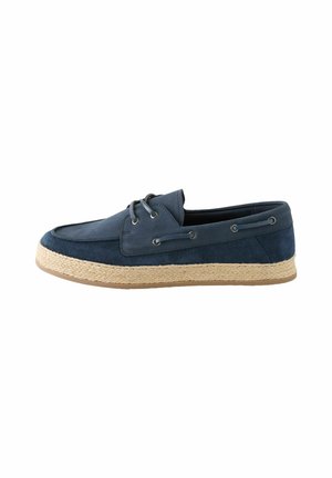 Men's navy blue suede boat shoe with beige woven sole and lace details on sides, shown in profile on white background.