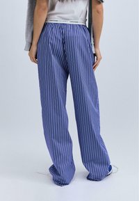 Un pantalon de pyjama à rayures bleues et blanches avec une coupe ample, une taille élastique et des poches latérales. Le matériau semble doux et léger.