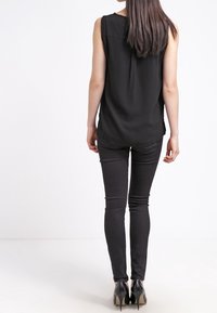 Svart ärmlös topp med avslappnad passform, tillsammans med slim-fit svarta byxor och högklackade skor; mjuk textur och enkel design.