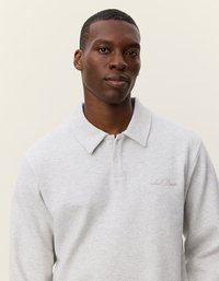 Világosszürke póló, puha anyagból készült, klasszikus gallérral, három gombbal és hímzett logóval a mellkason.