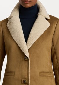 Giacca in suede marrone con colletto in sherpa beige, due bottoni e tasche laterali, caratterizzata da una morbida texture e design strutturato.