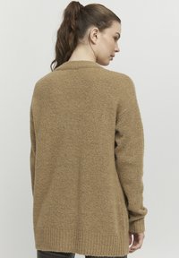 Beige lång kofta i mjuk, texturerad stickning. Har ribbad nederkant och ärmslut, med en avslappnad passform och bred ryggdesign.