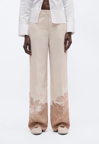 Bēšas plaša piegriezuma bikses ar ziedu rakstu maigi rozā un brūnās nokrāsās. Gluda auduma ar detalizētām ziedu kontūrām apakšmalā. Taisna priekšpuse.