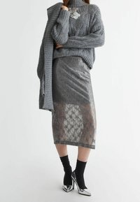 Grau gestrickter Pullover mit hohem Kragen und Strukturmuster, kombiniert mit einem glitzernden grauen Midikleid mit geometrischem Design. Silberne Absätze.
