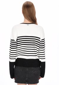 Suéter de punto a rayas blancas y negras con mangas largas y parte inferior negra sólida. Textura acanalada con un ajuste relajado.