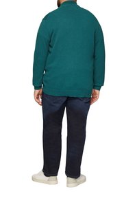 Türkiser Strickpullover mit hohem Kragen, gerippten Bündchen und Saum. Kombiniert mit dunkelblauen Jeans und weißen Sneakern, die einen lässigen Schnitt präsentieren.
