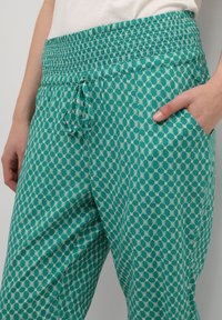 Turkosa mönstrade byxor har en smockad midja med dragsko, sidofickor och ett lätt tyg med ett geometriskt mönster.