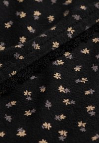 Tessuto nero con piccoli motivi beige e grigi a forma di quadrifoglio e una cucitura testurizzata che attraversa diagonalmente.