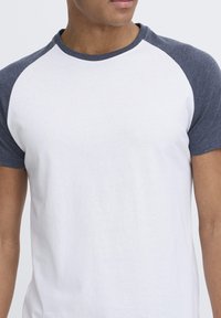 T-shirt with white body and navy blue raglan sleeves. Crew neck; soft, smooth fabric with a casual fit. No patterns or embellishments.