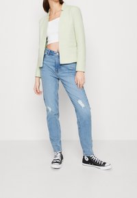 Veste courte vert clair, crop top blanc, jeans bleu clair déchirés, et baskets montantes noires. Style décontracté et ajusté avec des éléments classiques.