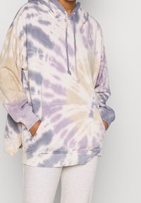 Felpa con cappuccio tie-dye che presenta tonalità pastello di viola, beige e crema, con cappuccio regolabile, maniche lunghe e tasca frontale.
