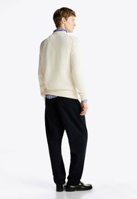 Cream-colored knitted sweater, relaxed fit, ribbed hem and cuffs, paired with dark navy loose-fitting pants and black loafers.