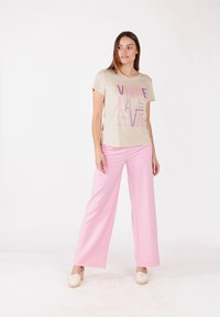 T-shirt beige avec texte imprimé en rose et violet, associé à un pantalon rose à jambes larges. Tissu lisse, coupe décontractée, sans motifs visibles.