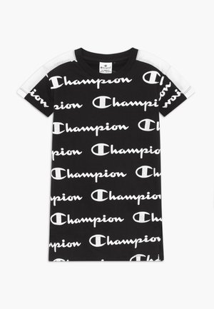 Czarna sukienka w stylu t-shirt z krótkim rękawem, z powtarzającym się białym napisem "Champion" na tkaninie oraz białymi panelami na ramionach i rękawach.