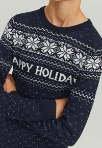 Námořnický pletený svetr s bílými vzory sněhových vloček a textem "ŠŤASTNÉ VÁNOCE". Ribbené manžety a lem, texturovaná látka s malými bílými tečkami.