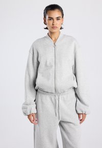 Sweat-shirt gris à fermeture éclair en tissu doux avec un col rond, des manches raglan et des poignets élastiqués, associé à un pantalon de jogging gris assorti.