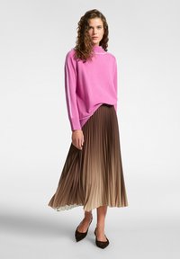 Maglione rosa a maglia con collo alto e polsini a costine abbinato a una gonna plissettata marrone con effetto ombre. Indossato con scarpe con tacco scuro.