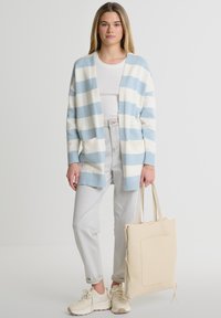 Juostuota kardiganas šviesiai mėlynos ir kreminės spalvos, atvira priekinė dalis su kišenėmis, derinama su šviesiomis džinsinėmis kelnėmis ir šviesiai rudos spalvos rankine. Minkšta mezgimo tekstūra.