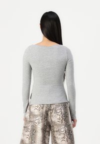 Grijze lange mouwen shirt met een ronde halslijn en een slim fit, gecombineerd met brede broek van slangenprint met patroon. De textuur lijkt zacht en glad te zijn.