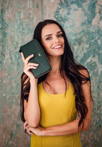 Green crocodile-embossed wallet with gold zipper and logo, held against a textured backdrop. Features smooth leather texture and sleek design.