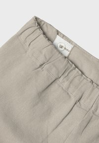Tessuto grigio chiaro con una vita arricciata e finitura elastica, e un singolo bottone decorativo nella parte superiore. Texture liscia.