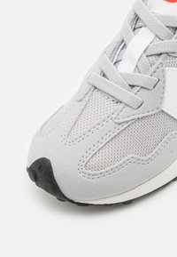 Sneaker gris mettant en avant un mélange de matériaux en daim et en mesh, avec une semelle en caoutchouc noire et des lacets ton sur ton. Lignes de design notables et variations de textures.