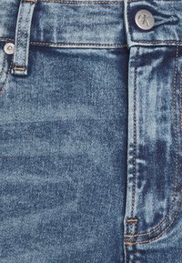 Light blue denim jeans featuring subtle whiskering, a button closure with a logo, and contrasting orange stitching along the seams.