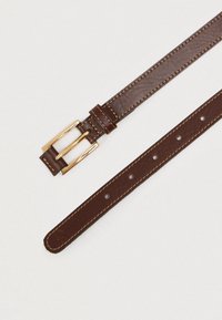 Ruskea nahkavyö kultaisella soljella. Ominaisuuksiin kuuluu vaaleat tikkaukset, säätöreiät ja sileä pinta.