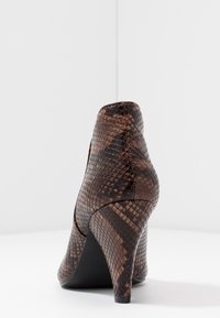 Zapato de tacón alto con un exterior de estampado de serpiente en tonos marrón y negro, con textura. Presenta una punta afilada y un diseño de tacón curvado.