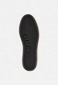 Soletta per scarpe nera con la scritta "GUESS" impressa in lettere scure. Presenta una superficie testurizzata e bordi arrotondati per il comfort.