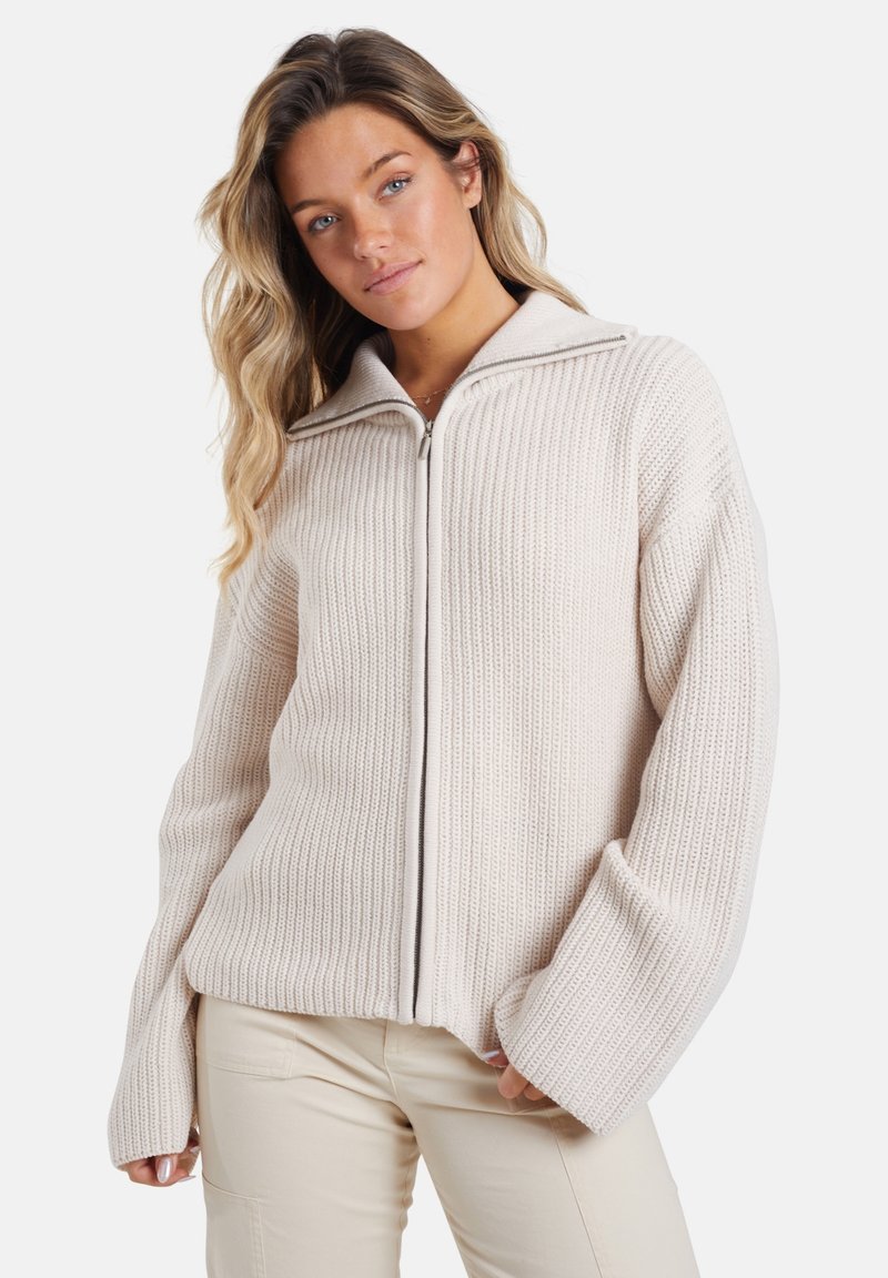 Langsleeve, lichtbeige gebreide trui met een ritsafsluiting en een geribbelde textuur. Voorzien van een brede kraag en een oversized, relaxte pasvorm.