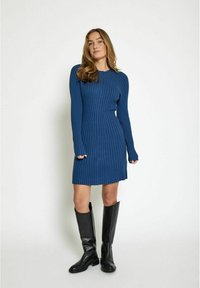 Vestito blu a coste con maniche lunghe e scollo rotondo, abbinato a stivali neri in pelle al ginocchio. Vestibilità slim con texture verticale.