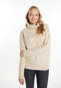Beige kabelgebreide trui met een hoge, geribbelde col. Kenmerkt zich door een losse pasvorm en heeft geribbelde manchetten en zoom. Draagt met donkere jeans.