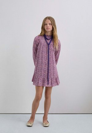 Vestido de patrón morado y rosa con un dobladillo acampanado, mangas largas y un detalle de lazo en el escote. Tejido suave; combinado con bailarinas doradas.