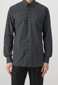 Camicia a maniche lunghe in tessuto nero con un motivo bianco ripetitivo. Presenta un colletto a camicia e polsini, con un design slim fit.