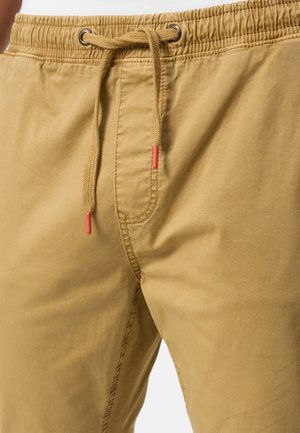 Lys brun shorts med snor i midjen, med sølvøyler og røde topper. Mykt, glatt stoff og en avslappet passform.