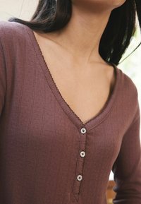 Långärmad, mauve V-ringad topp i texturerad tyg. Har en knapplist med fyra vita knappar och delikat scalloped trim.