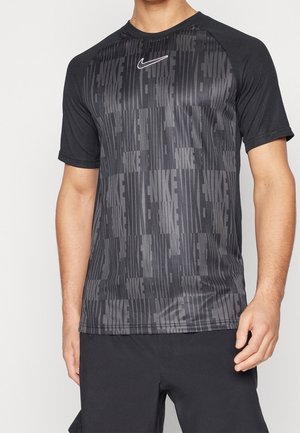 Homme portant un t-shirt de sport noir Nike avec un motif vertical répétitif du texte Nike et un petit logo swoosh blanc Nike sur la poitrine.