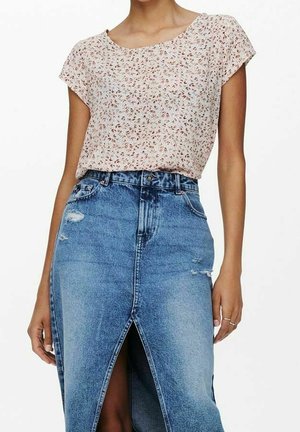 Mujer con blusa de manga corta con estampado floral, metida dentro de una falda de mezclilla azul de talle alto con una abertura frontal y detalles desgastados.