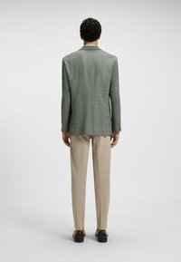Ljusgrön rutigt kostymjacka med notch-lapel. Kombination med beige byxor och mörka skor. Slät textur, skräddarsydd passform, strukturerad design.