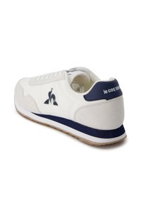 Scarpa sportiva bianca con accenti blu marino, materiali in suede e pelle, design con lacci, suola in gomma e dettaglio del logo sul lato e sul tallone.