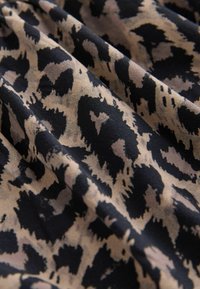 Tissu doux avec un motif léopard beige et noir irrégulier, montrant de légers plis et de la texture.